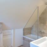 Bathroom with shower, sink, and heater under sloped ceiling