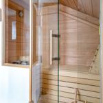 Sauna with wooden walls and glass door, wooden bench and bucket with ladle