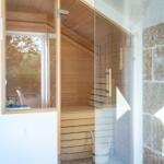Sauna with wooden walls and bench, separated by glass wall.