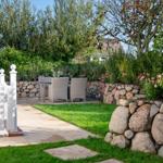 Backyard with white fence, stone wall, and seating area in garden.