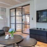 Living room with fireplace, glass doors, and TV. Round tables and seating area.