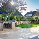 Terrace with garden, table and chairs. Backyard with stone wall and grass.