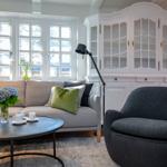 A living room with sofa, armchair, table, and windows.