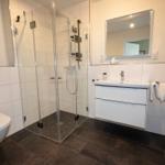 Badezimmer mit Dusche, Waschbecken und Toilette. Fliesenboden und Spiegelschrank.