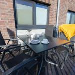 Terrasse mit Tisch, Stühlen und gelber Decke vor Backsteinhaus