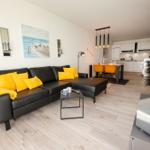 Schwarzes Sofa mit gelben Kissen, Essbereich und Küche im Hintergrund.