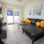 Wohnzimmer mit schwarzer Couch, gelben Kissen und Blick auf Balkon.