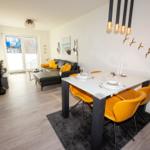 Essbereich mit gelben Stühlen und Esstisch. Wohnbereich mit Sofa und Terrassentür.