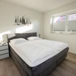 Schlafzimmer mit Doppelbett, Nachttisch und Fenster mit Blick auf Dächer.