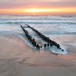 Sunset over the sea with wooden posts in the foreground.