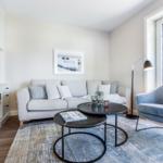 Living room with sofa, armchair, and table. Window view of house and roof.