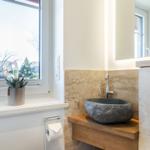 Bathroom with stone basin, wooden vanity, and window view of outdoor area.