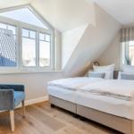Bedroom with double bed, blue armchair, and large windows.