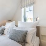 Bedroom with sloped ceiling, window, and bed with pillows.