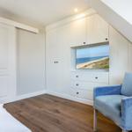 Bedroom with sea view, blue armchair, and white wardrobes.