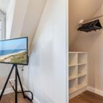 A room with window, TV on stand, and closet with hangers.
