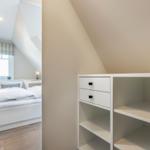 Bedroom with sloped ceiling, white bed, and cabinet with drawers.