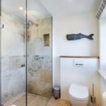 Shower with glass enclosure, toilet, and window with fish decoration.