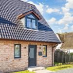 House with brick facade and dark roof, entrance door and windows.