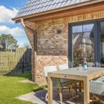 Terrace with wooden table and chairs beside brick house with garden gate.