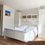 Schlafzimmer mit weißem Bett, Schränken und Wandbild.