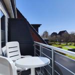 Balkon mit weißem Tisch und Stühlen, Blick auf Wohnhäuser und Grünflächen.