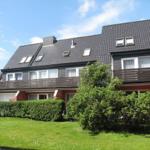 Modernes Mehrfamilienhaus mit Balkonen und Dachfenstern. Grünflächen und Hecken im Vorgarten.
