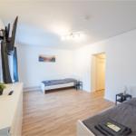 Zimmer mit zwei Betten, Holzboden und TV. Kleine Garderobe im Hintergrund.
