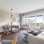 Wohn- und Essbereich mit Sofa, Tisch und Fernseher. Durchgang zur Terrasse mit Blick auf Grünfläche.