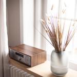 Auf einem Fensterbrett steht ein Radio und eine Vase mit getrockneten Pflanzen.