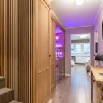 Halle mit Holztreppe, Spiegeln und Lampen. Durchgang zu Wohnzimmer und Sauna.