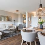 Wohn- und Essbereich mit Sofa, Tisch und Stühlen. Holzboden und moderne Beleuchtung.