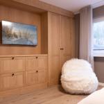 Schlafzimmer mit Holzmöbeln, Fernseher und flauschigem Sitzkissen.