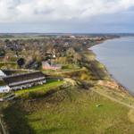 Haus mit Grasdach am Wasser, Blick auf Küstenweg und Dorf.