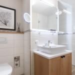 Badezimmer mit Dusche, Waschbecken und Toilette. Wand mit Bild und Holzregal.