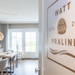 Tür mit Logo WATT PRALINE ESTD. 2022. Im Hintergrund Essbereich mit Tisch und Stühlen.