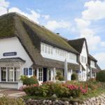 Weiße Villa mit Strohdach und Blumenbeet