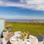 Terrasse mit Tisch, Stühlen und Blick auf das Meer.