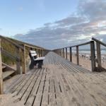 Holzpromenade führt zum Strand mit Strandkörben und Wellen.
