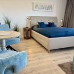 Schlafzimmer mit Bett, Tisch und Stühlen. Blaue Kissen und Wandbild.