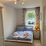 Schlafzimmer mit Bett, Nachttisch und Fenster mit Vorhängen.