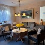 Wohnzimmer mit Sofa, zwei Sesseln, Tisch mit Blumen und Wandbild.