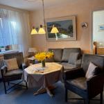 Wohnzimmer mit Sofa, zwei Sesseln, Tisch und Blumen. Wandbild und Deckenleuchte sichtbar.