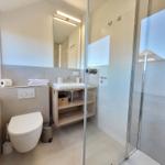 Badezimmer mit Dusche, Waschbecken und Toilette. Fenster mit Jalousie.