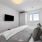 Schlafzimmer mit Bett, TV und Fenster. Holzboden und weißer Kleiderschrank.