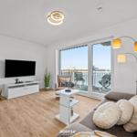 Wohnzimmer mit Sofa, Fernseher und Balkonansicht.