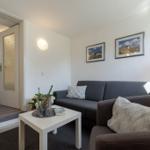 Wohnzimmer mit Sofa, Tisch und Bildern. Tür führt in Schlafzimmer.