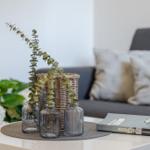 Tisch mit Vasen, Pflanzen und Buch vor Sofa