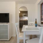 Essbereich mit Tisch, Stühlen und Fernseher. Küche im Hintergrund sichtbar.