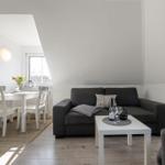 Wohn- und Essbereich mit grauem Sofa, weißem Tisch und Holzboden.